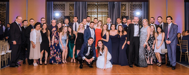 Large group of people stand behind a crouching bride and groom.